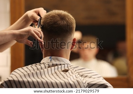 A young male Barber adjusts the hair of a male client. Professional hair care products. Cinematic close-up of a barber giving fade haircut to male client. shot of short clipper hairstyle. Royalty-Free Stock Photo #2179029579