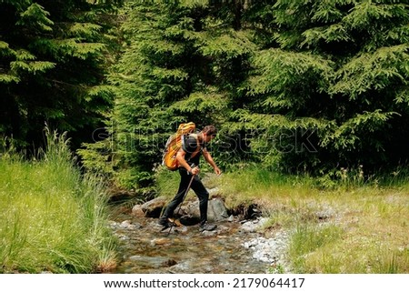 rear view of a tourist young man with a backpack travels through the forest near the river. young man equipped with tourist equipment hiking, lifestyle. active life mode, active rest Royalty-Free Stock Photo #2179064417