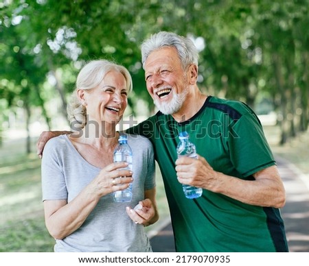 Smiling active senior couple holding water bottles, drinking and  jogging together in the park Royalty-Free Stock Photo #2179070935