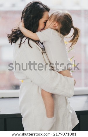 Mom and daughter in white gently hug and kiss