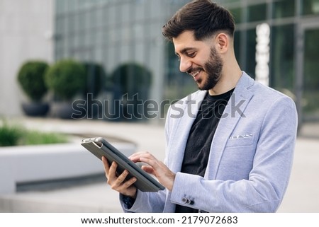 Beautiful young man engaged in business using tablet computer reading financial news online. European hairstyle. Corporate people.