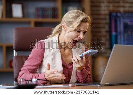 Furious businesswoman shouting expressively to smart phone while answering phone call at office. Angry annoyed woman enraged of bad service, having problem with not working mobile phone, get spam Royalty-Free Stock Photo #2179081141