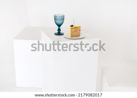The yellow piece of lemon slices birthday cake withe blue glasses on white cube table. Minimalist holiday party objects. Celebrating.