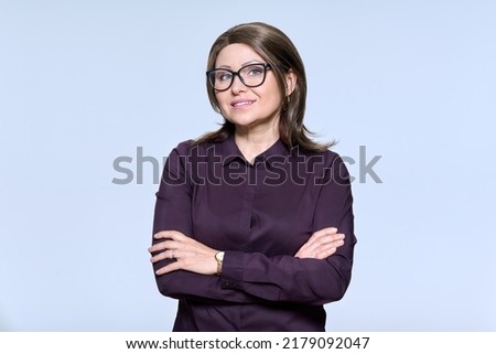 Portrait of confident mature woman in glasses looking at camera on light background