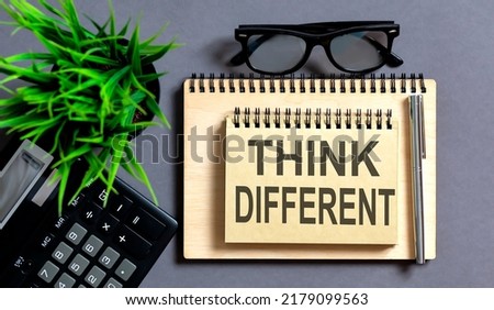 Word THINK DIFFERENT on a notebook with pencil on grey background