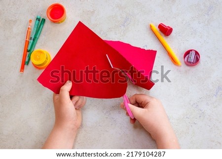 Child cuts out big red heart. St. Valentines day theme. Crafts concept. Kid makes art art project 