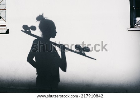 Beautiful and fashion young woman posing with a longboard. Photo of shadows of girl with a skateboard. Horizontal