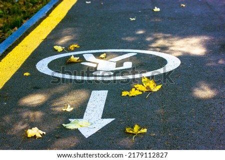 Asphalted road, path with yellow markings, circular pictogram sign with the image of a person, allowing safe walking in an autumn park, forest at the resort. White arrow indicating direction forward.