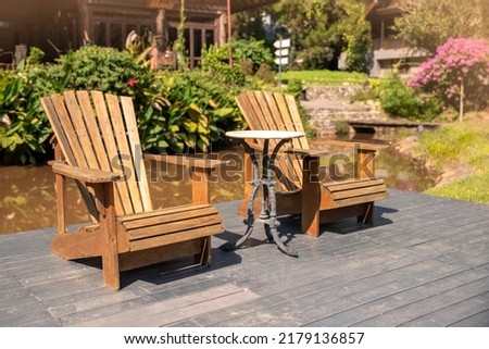 Two armchairs, wooden garden furniture on wood floor outdoor for relaxing on summer days. Garden landscape with two chairs in nature, flowers in vase.. Backyard exterior. holiday concept