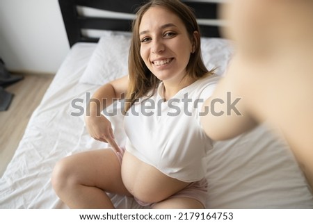 Self-portrait, above high angle view of lovely excited cheerful pregnant mom in casual wear sitting on bed, couch, white light interior room, webcam view