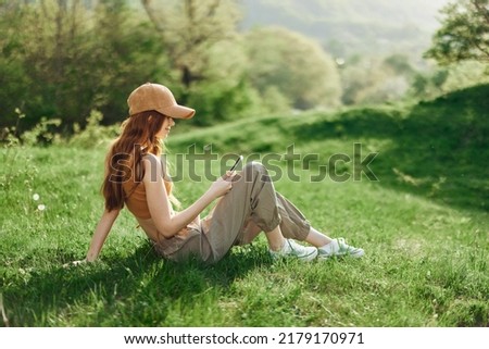 Bottom view young student freelancer woman in green jacket jeans sit on bench in spring park outdoors talk by mobile cell phone look aside. People urban lifestyle concept Royalty-Free Stock Photo #2179170971
