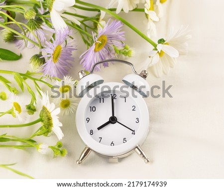 Good morning card with wild flowers and alarm clock on a white textile background. Fine way to start a day. The concept of a good sleep, easy awakening and a good start to the day