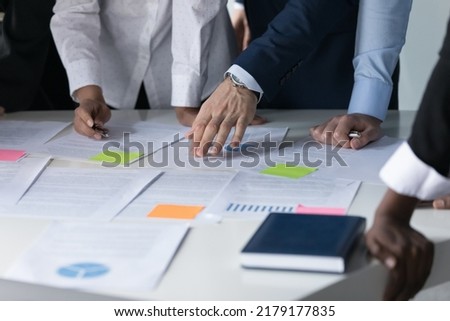 Meeting table and hands of multiethnic business colleagues close up. Team of businesspeople discussing paper reports with sticky notes, analyzing marketing, statistic data, working on project together Royalty-Free Stock Photo #2179177835