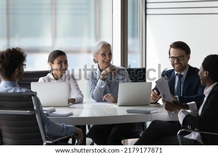 Happy cheerful diverse different aged business team negotiating in meeting room, brainstorming at round table, talking, discussing reports, startup project, laughing at joke, having fun Royalty-Free Stock Photo #2179177871