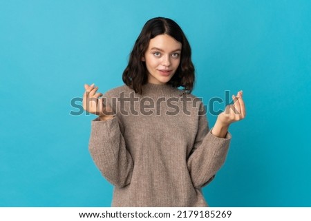 Teenager Ukrainian girl isolated on blue background making money gesture