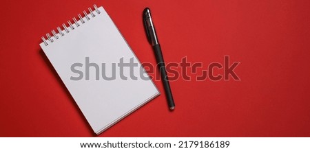 Open notebook on a spring and a black ballpoint pen on a red background copy space