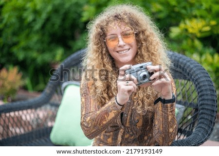 Woman with curly hair dressed in vintage clothing holding a vintage camera 