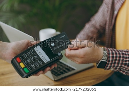 Cropped young man he wear shirt hold wireless bank payment terminal to process acquire credit card payments sit at table in coffee shop cafe rest in free time. Freelance mobile office business concept Royalty-Free Stock Photo #2179232051