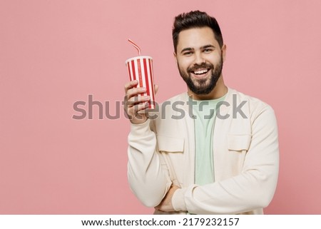 Young smiling cheerful fun happy caucasian man 20s wear trendy jacket shirt hold soda cola cup of fizzy water isolated on plain pastel light pink background studio portrait. People lifestyle concept