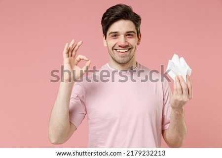 Sick ill ailing allergic man has red eyes runny nose suffer from allergy hold paper napkin isolated on pastel pink color wall background studio Healthy lifestyle disease treatment cold season concept Royalty-Free Stock Photo #2179232213