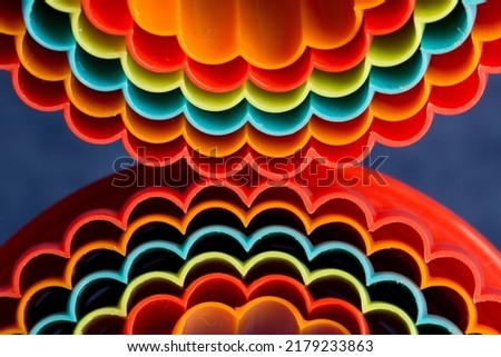 A macro closeup abstract image of colourful plastic pastry cutters.  Looking end-on the red, orange, green and blue wavy edges are reflected beneath against a blue background.