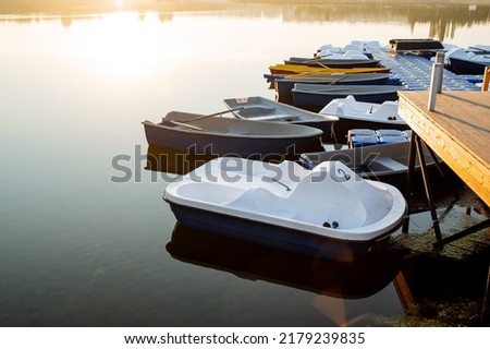 Calm water boat dock, morning dawn glare of the sun, white catamaran for river walks, boat rental in the park, city pond. High quality photo