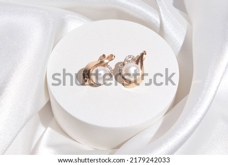 Pearl earrings with golden fittings on shiny beige silk background. Beautiful accessories for women. Elegant jewelery gift or present for wedding or saint valentine's day. Royalty-Free Stock Photo #2179242033