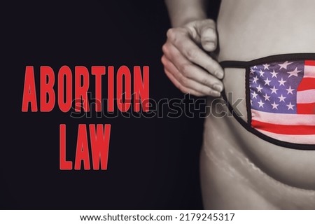The inscription abortion law and pregnant woman on black background with medical mask and usa flag. The concept of problems with coronavirus during pregnancy