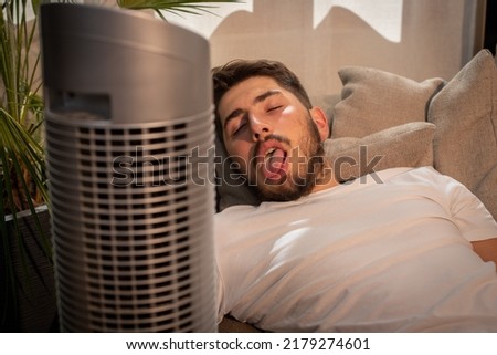 funny image of a young man lying in his sofa suffering from the heat. In the foreground, a fan that cools it during the heat wave
 Royalty-Free Stock Photo #2179274601