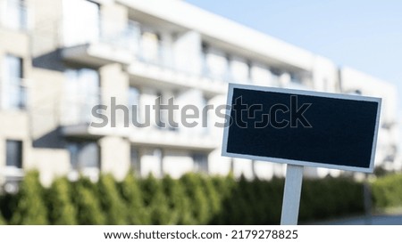 Blank Black billboard against new apartment building Empty mockup template Blackboard label Home for rent. Apartments for sale. Sign in front of new home. Copy space for Advertisement