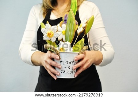 A woman in a black apron shows a dessert in the form of gingerbread flowers to the camera. Horizontal photo
