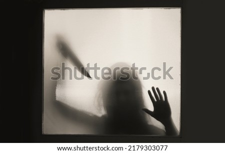 Horror, halloween background - Shadowy figure behind glass holding a knife