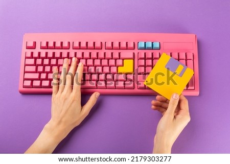 Hand holding floppy disk on color keyboard background, technology concept. High quality photo