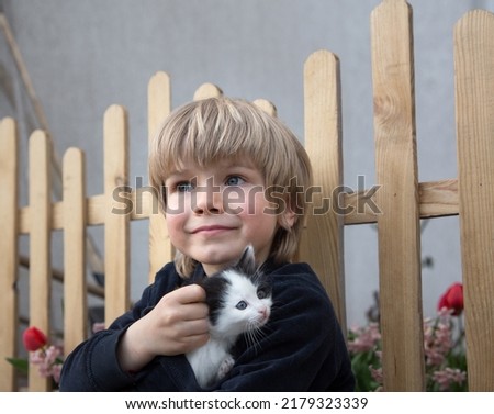 boy of 5 years old carefully holds in his hands a small black and white beloved kitten. cat day. Happy childhood with a fluffy pet. Royalty-Free Stock Photo #2179323339