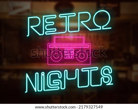 A retro nights neon sign in front of a bar or pub. A pink cassette player graphic. Nightlife throwback 70s 80s 90s party concept. Neon pink and teal colors.