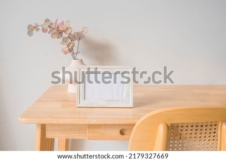 Portrait white picture frame mockup on wooden table. Modern ceramic vase with eucalyptus. White wall background. Scandinavian interior.  