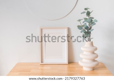 Portrait white picture frame mockup on wooden table. Modern ceramic vase with eucalyptus. White wall background. Scandinavian interior.   Royalty-Free Stock Photo #2179327763