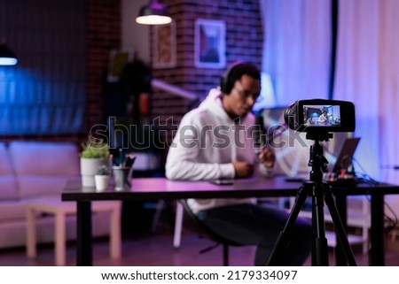 Modern person filming podcast episode on camera in studio, live broadcasting online discussion to create social media content. Male influencer vlogging show with livestream equipment.