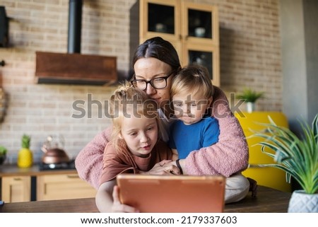 Happy young mother and two kids, little daughter and baby son, watching cartoons on tablet computer. Loving family enjoying time together at home, mom hugging children