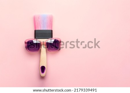 Paintbrush in sunshine safety glasses on pink background with copy space. Creative concept.