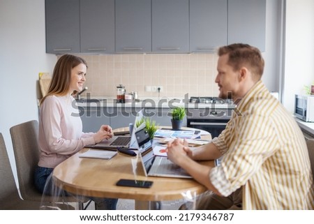 Side view of young couple working from home on laptops sitting together at table. Wife and husband discussing business while working remotely or as freelancers Royalty-Free Stock Photo #2179346787