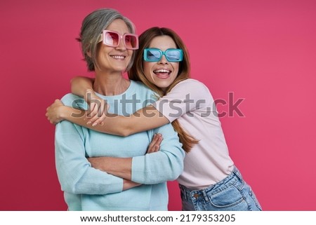 Happy daughter embracing her senior mother against pink background