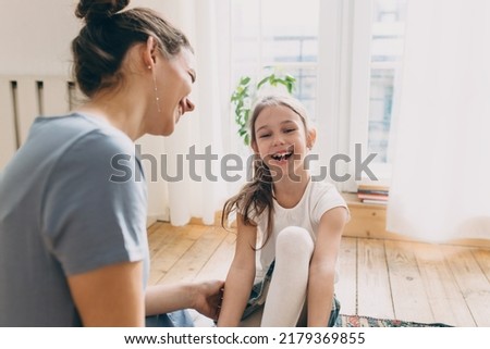 Selective focus of funny laughing 7-years-old girl sitting on floor in white blouse and denim skirt next to her elder sister, talking, having fun. Conscious parenting. Happy , carefree childhood Royalty-Free Stock Photo #2179369855