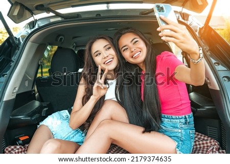 Beautiful asian girls friends have fun and taking selfie on smartphone camera while sitting at the car trunk. Travel, happy lifestyle, good mood concept.