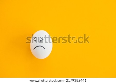 Egg with sad face on yellow background