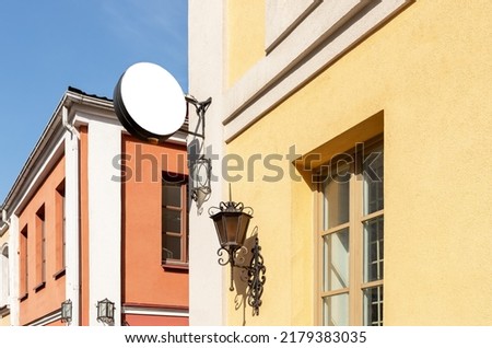 Round signboard mockup at old city building with retro lantern. White template for displaying cafe, restaurant, shop, museum, hotel name or logo. High quality photo