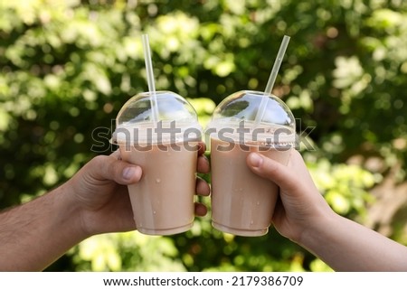 Man and woman toasting with plastic takeaway cups of delicious iced coffee outdoors, closeup Royalty-Free Stock Photo #2179386709