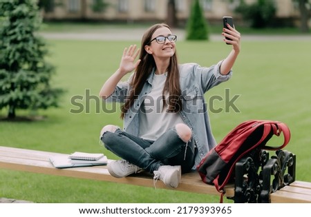 Cute student girl near campus taking selfie and live streaming video on social media