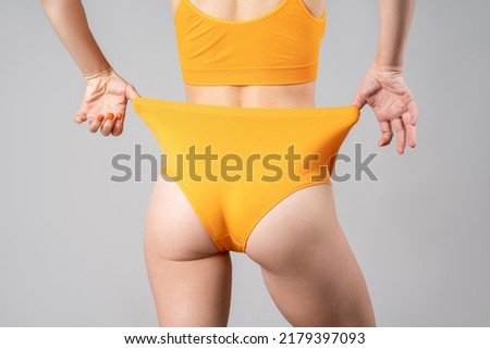 Slim woman in yellow underwear after weight loss on gray background, body care concept