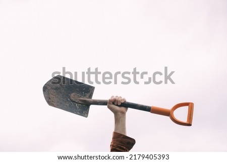A man's hand holds a bayonet shovel on a white background. Metal shovel in his hands against the sky Royalty-Free Stock Photo #2179405393